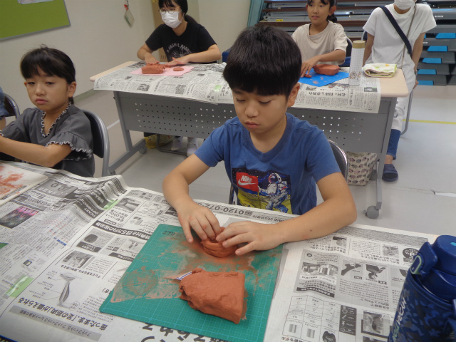 ひも状の粘土を土器に積み上げる子ども