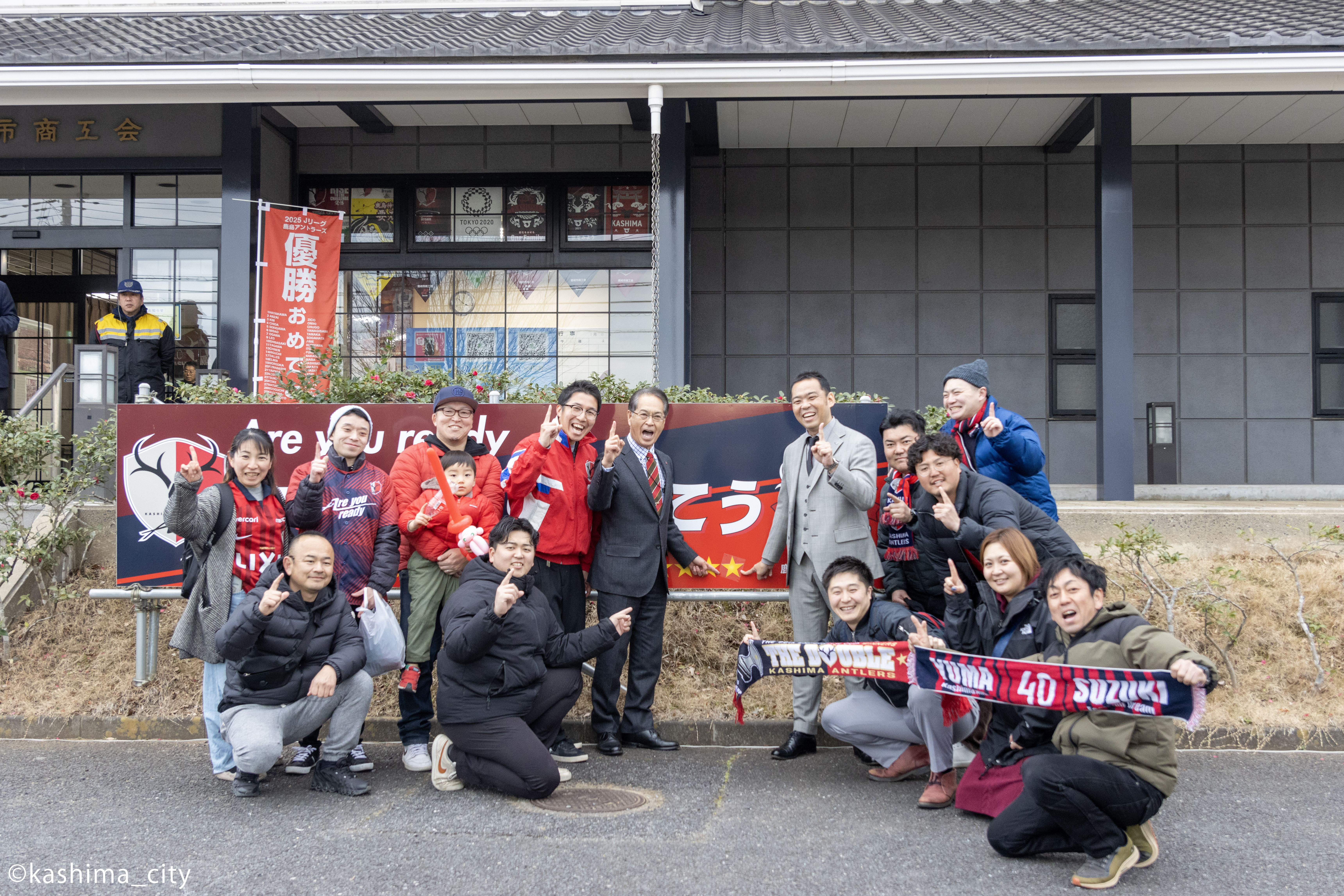 アントラーズの看板を囲む小泉社長と商工会会員の皆さん