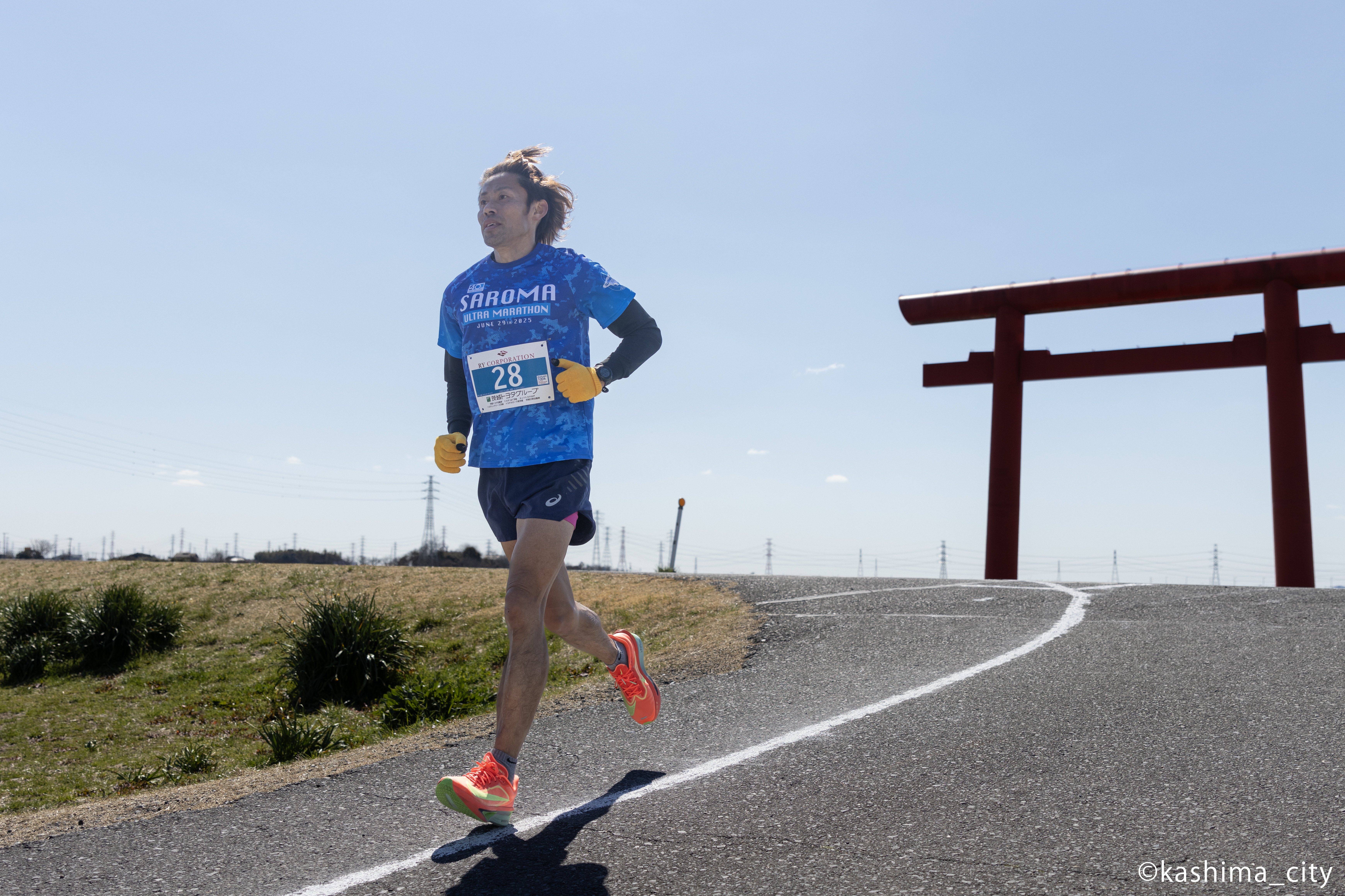 鳥居を背に走る髪をしばった男性