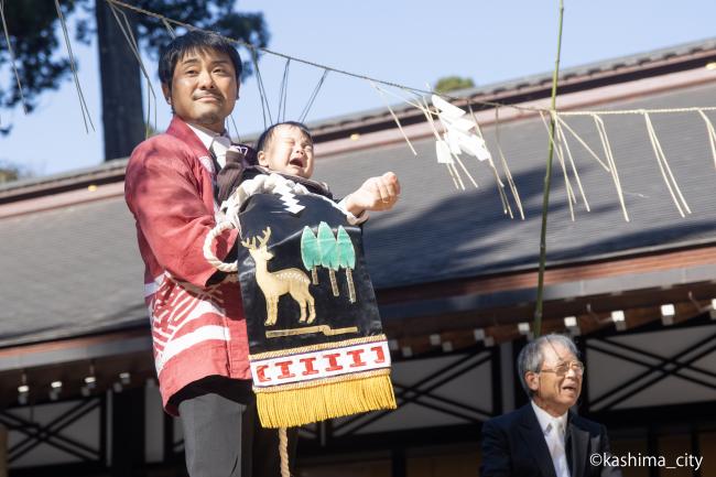 子どもが介添え役に抱きかかえられて土俵入りする様子